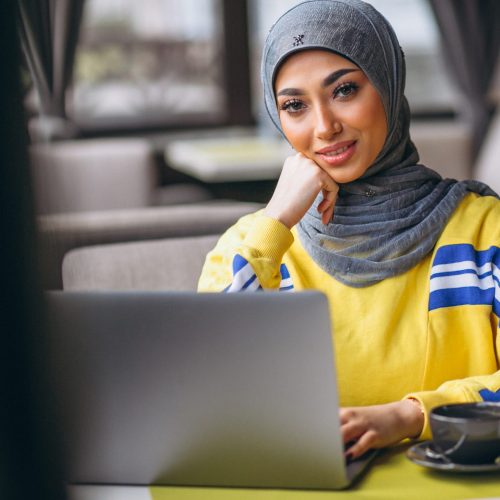 Arabian woman in hijab inside a cafe working on laptop